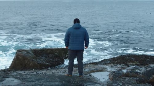 A Man Stands on a Rocky Shore and the Sea Waves Break on the Rocks