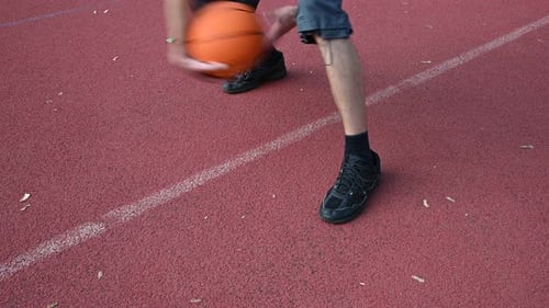 Homme dribblant un ballon de basket sur un court rouge