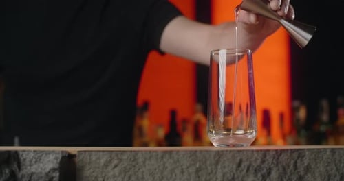 Barkeeper gießt in Zeitlupe eine Portion Alkohol vom Jigger in das Cocktailglas und macht den
