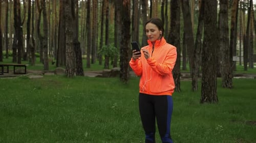 Sport female athlete wearing earphones and using training app on smartphone before running in park