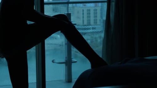 Silhouette of Woman Putting on Stockings in City Apartment