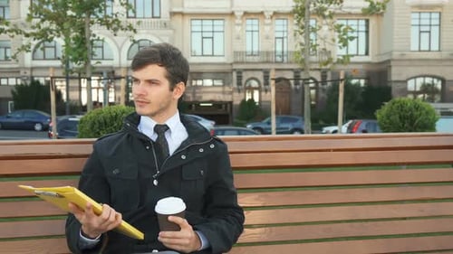 Man Sits on Bench with Coffee and Clipboard