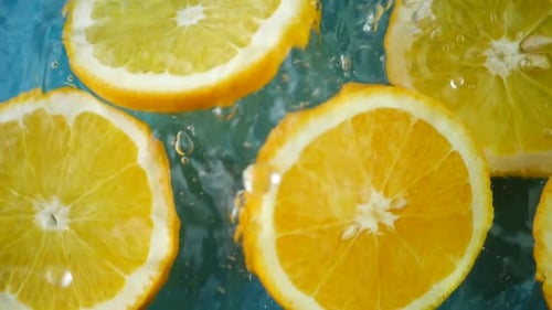 Group of Fresh Orange Fruit Slice Falling in Water on Blue Background