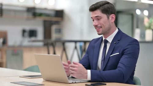 Cheerful Businessman Talking on Video Call on Laptop in Office