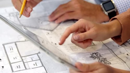 Businesswoman using digital tablet while coworker working on blueprint