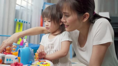 Asiatische glückliche Familie, schöne Mutter und kleines Mädchen spielen zusammen Spielzeug im heimischen Wohnzimmer