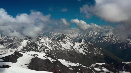 Air Flight Through Mountain Clouds Over Beautiful Snowcapped Peaks of Mountains and Glaciers