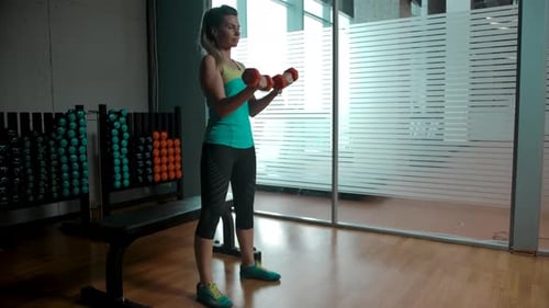 Caucasian Blonde Woman Doing Exercises for Biceps with Two Dumbbells in the Gym