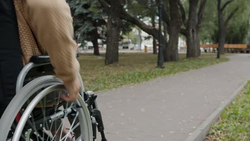 Dolly Shot of Handicapped Young Man Riding Wheelchair in City Street on Autumn Day