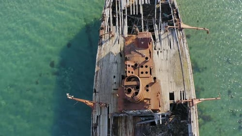 Ein zerstörtes Holzschiff liegt an der mit Rost bedeckten Küste
