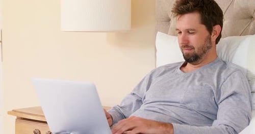 Man Relaxes in Bed Using Laptop