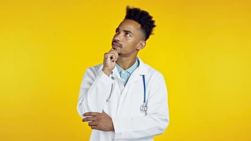 Thinking Black Doctor Man Looking Up and Around on Yellow Background. Worried Contemplative Face