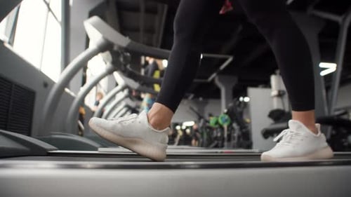 Closeup of Womans Legs in White Sneakers Walking on Treadmill in Gym Side View