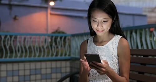 Woman Using Smartphone on Bench at Night