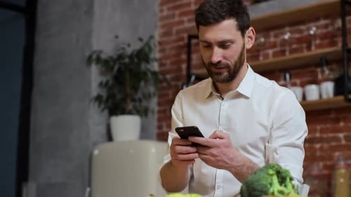 Man Using Smartphone in Kitchen near Fresh Food
