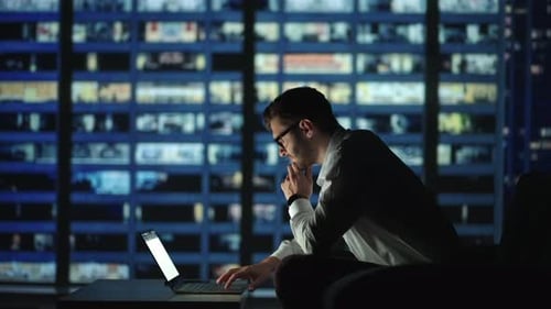 Focused Business Man Working on Laptop Computer Making Notes Sitting at Home Office Desk at Night