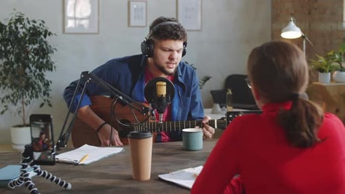 Man Singing and Playing Guitar in Recording Studio with Female Host