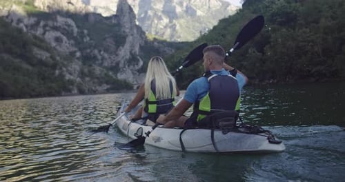 Couple Kayaking on Tranquil Lake Surrounded by Mountains