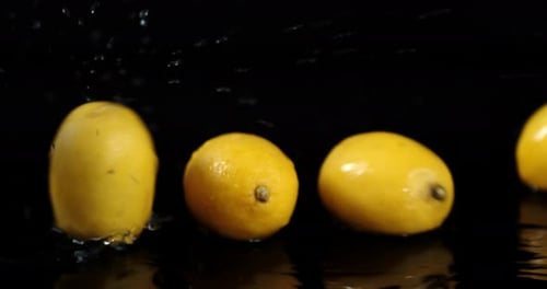 Fresh Lemons Falling onto Wet Black Surface