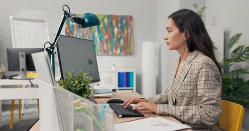 An Attractive Experienced Company Accountant Sits in Office in Front of a Computer Checking