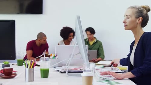 Femme travaillant sur un ordinateur de bureau avec des collègues en arrière-plan 4k