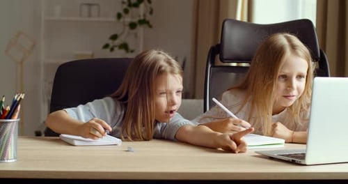 Two Happy Cute Little Friends Girls Sitting at Home Table or in Class, Remote Study with Laptop and