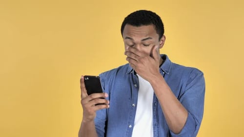Young Adult Shocked by Phone on Yellow Background