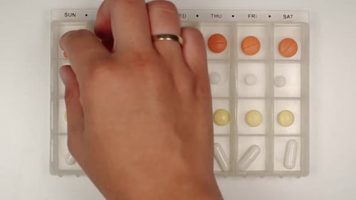 Hand Removes Pill from Weekly Organizer