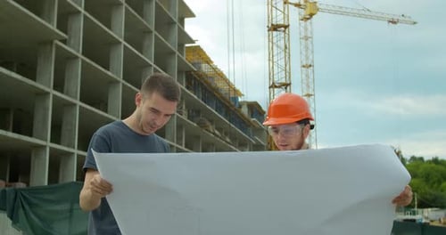 Builder with a Male Client Near Building Under Construction Outdoors. Two Male Builders Engineers