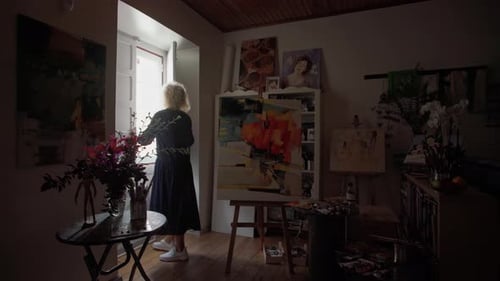A Middle Aged Woman Artist in a Dark Room of an Art Workshop Opens a Window