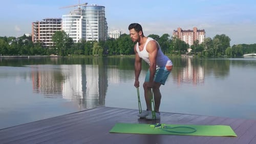 Athletic and Muscular Man Stretching Rubber Band Near Lake