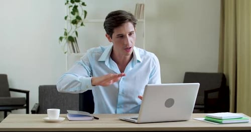 Busy Serious Man Sits in Office Home Room at Table with Laptop, Uses Webcam for Negotiations, Speaks