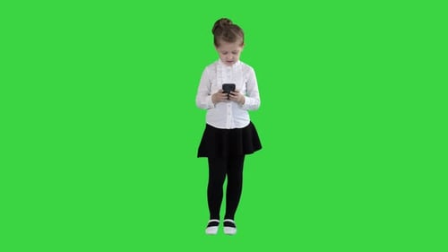 Cute Little Girl Looks in Smartphone and Writing a Message on a Green Screen, Chroma Key.