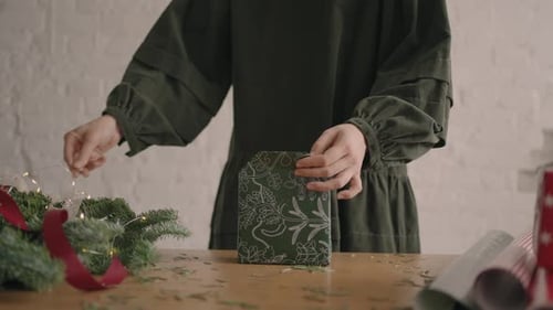 A Woman on a Wooden Table Decorates a Green Christmas Gift