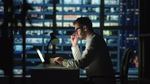 Tired Young Man Working on a Laptop Late Night in the Office