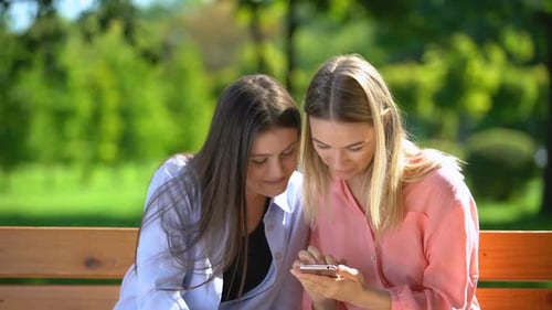 Two Women Smiling, Looking at Smartphone Outdoors