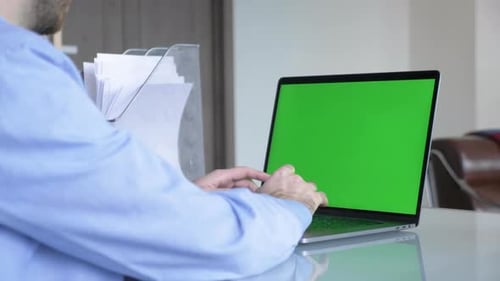 Man in the home office typing on laptop keyboard with green screen chroma mock-up