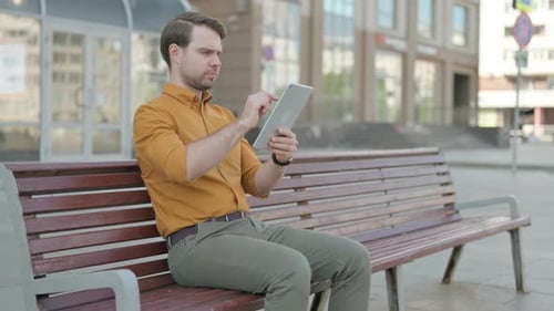 Man Using Tablet on Bench in Urban Setting