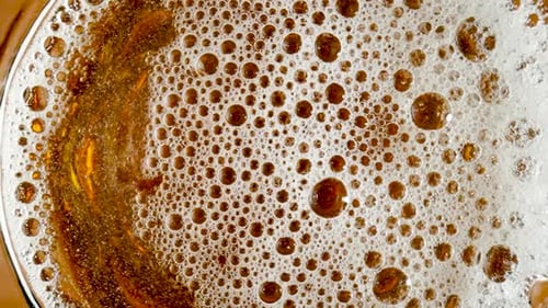 Top View of Golden Liquid in Glass with White Foam and Bursting Bubbles