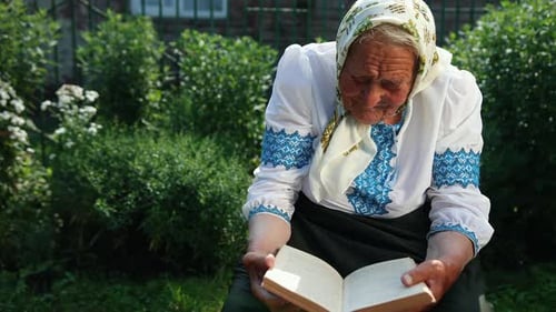 An Old Grandmother is Sitting on the Street and Reading a Book
