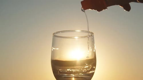 Pouring Water Into Glass at Sunset on the Beach