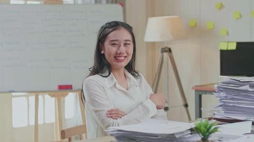 Asian Woman Crossing Arms And Smiling To Camera While Working With Documents At The Office