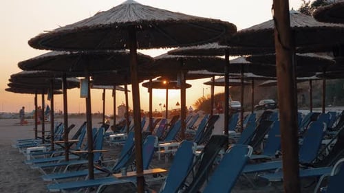 Beach with straw umbrellas and deck chairs at sunset, Greece
