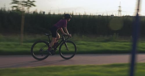Professional female cyclist athlete is speeding down the road on aero bike at sunset.