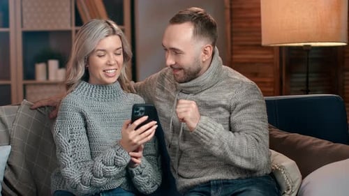 Excited Couple Watching Phone on Couch at Home