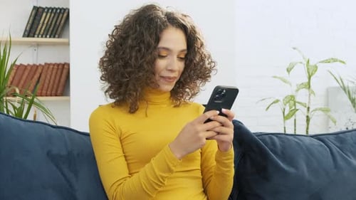 Woman Using Smartphone on Sofa at Home