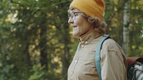 Elderly Woman Walking in Forest with Trekking Poles