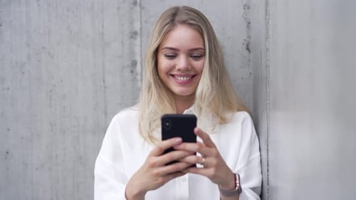 Smiling Woman Using Smartphone Leaning on Wall
