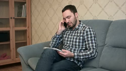 Young Man Using Tablet While Talking on Phone