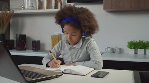 Cute School Age African American Girl in Headphones e Learning Using Laptop Pc at Home